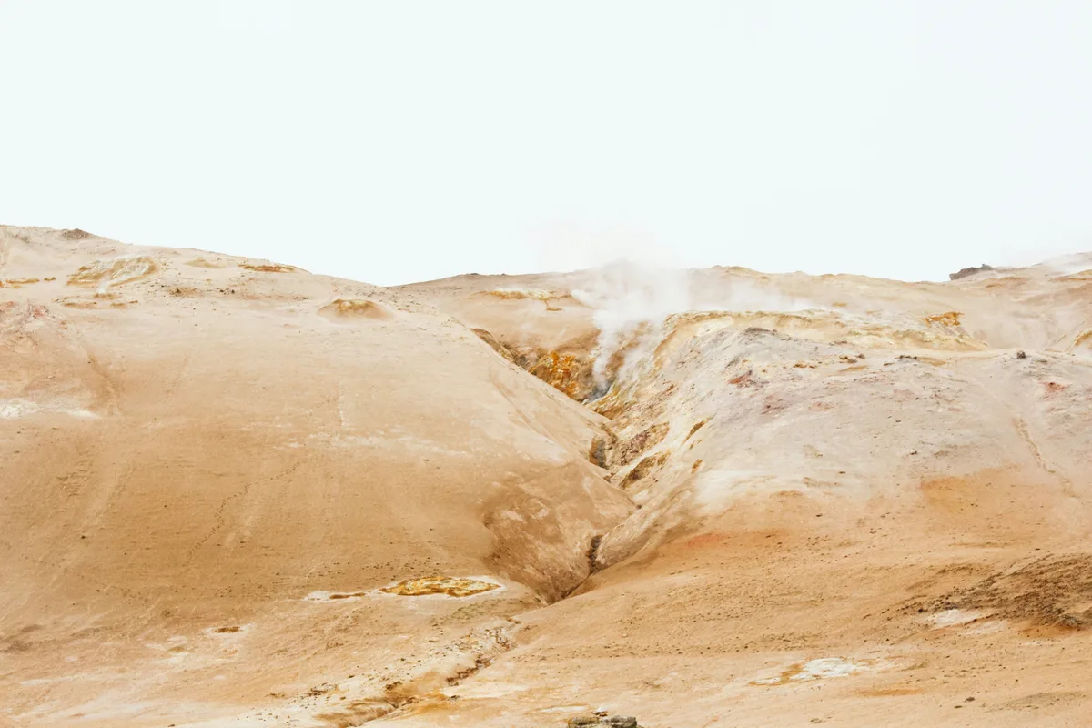 明るいオーカー色の丘に、地熱地帯の噴気が立ちのぼる写真